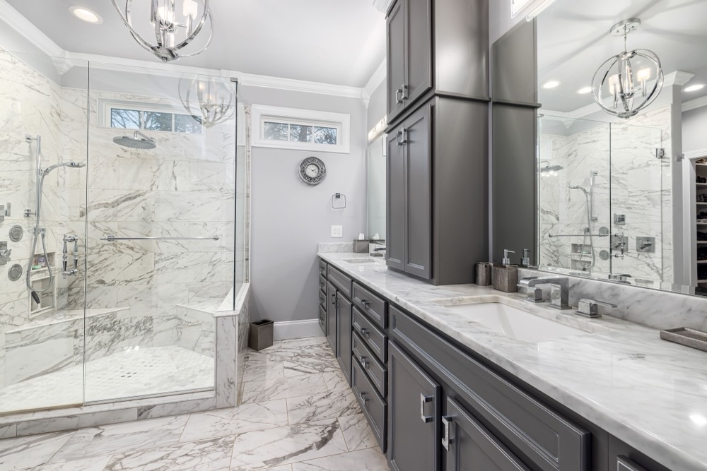 A remodeled bathroom with marble tile walls, a glass walk-in shower, and a double vanity
