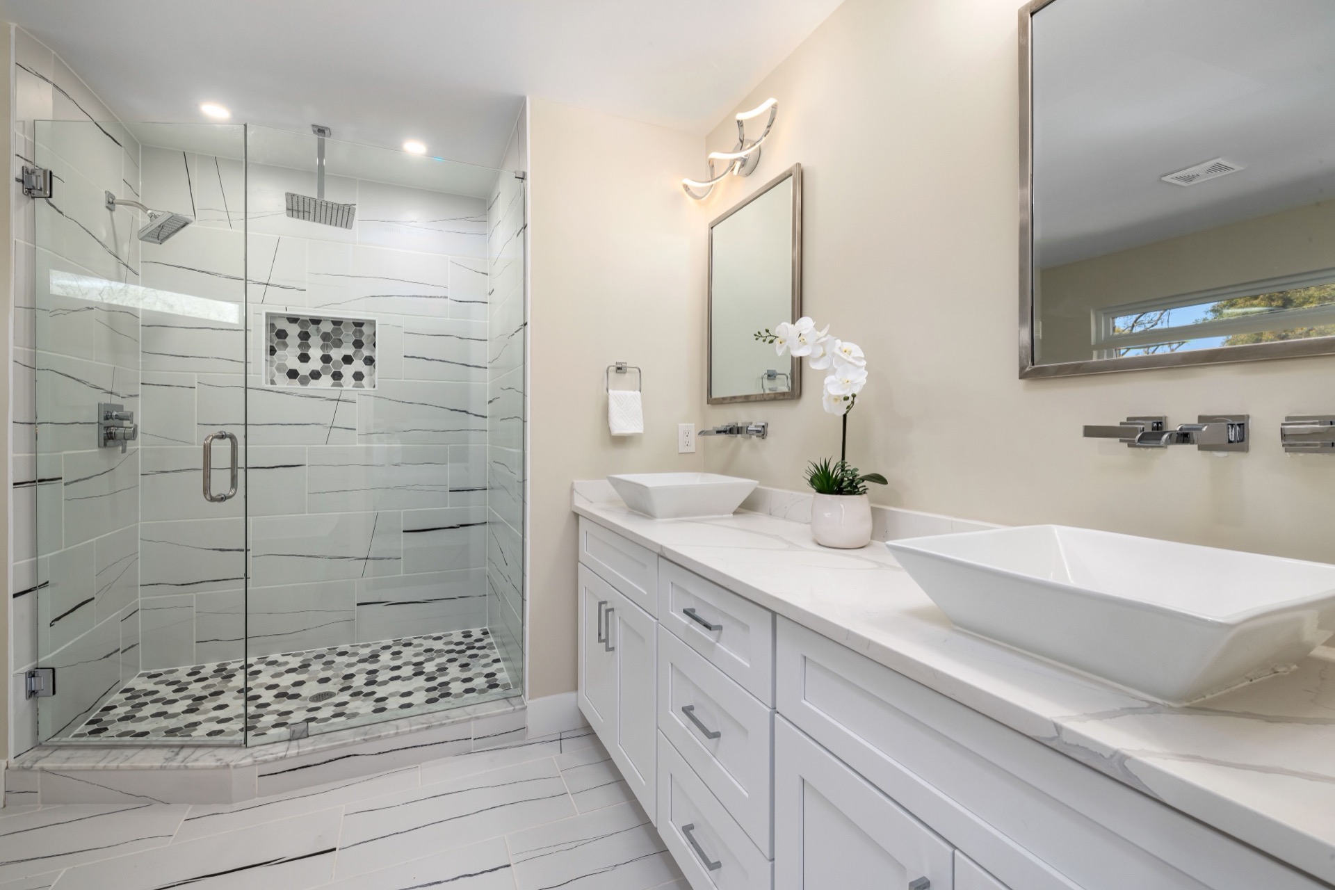 A bright, remodeled bathroom with a double vanity, quartz countertops, and a glass walk-in shower