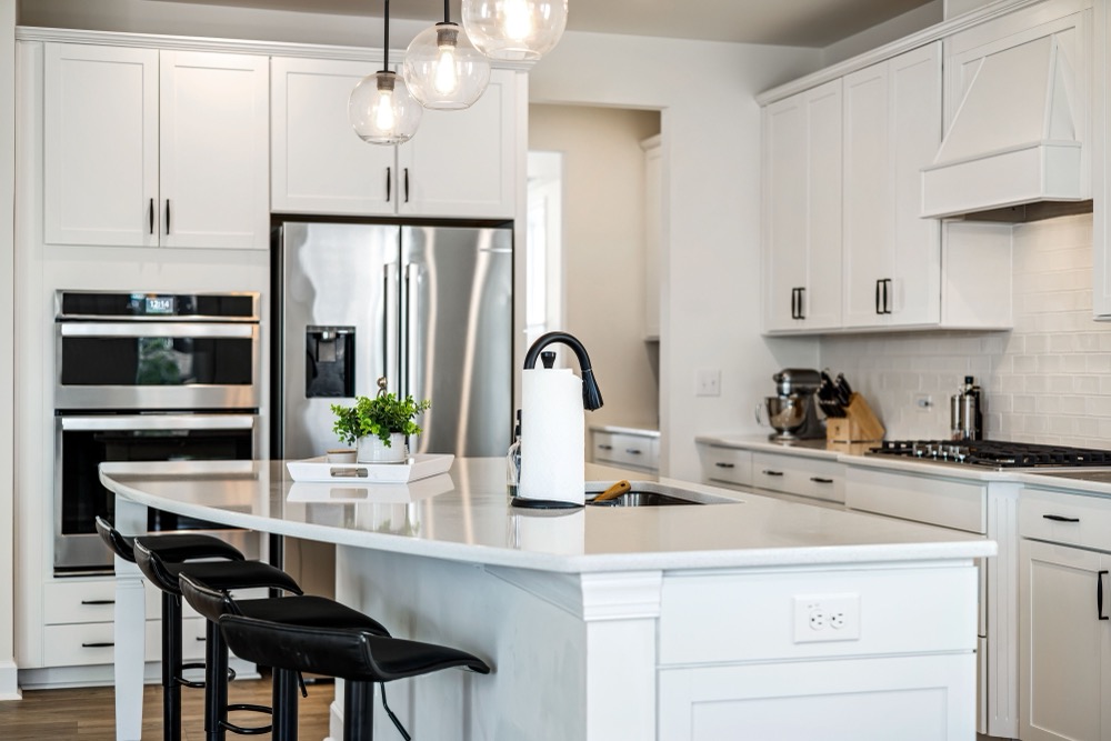 A bright modern kitchen with a white quartz island, pendant lighting, and stainless appliances